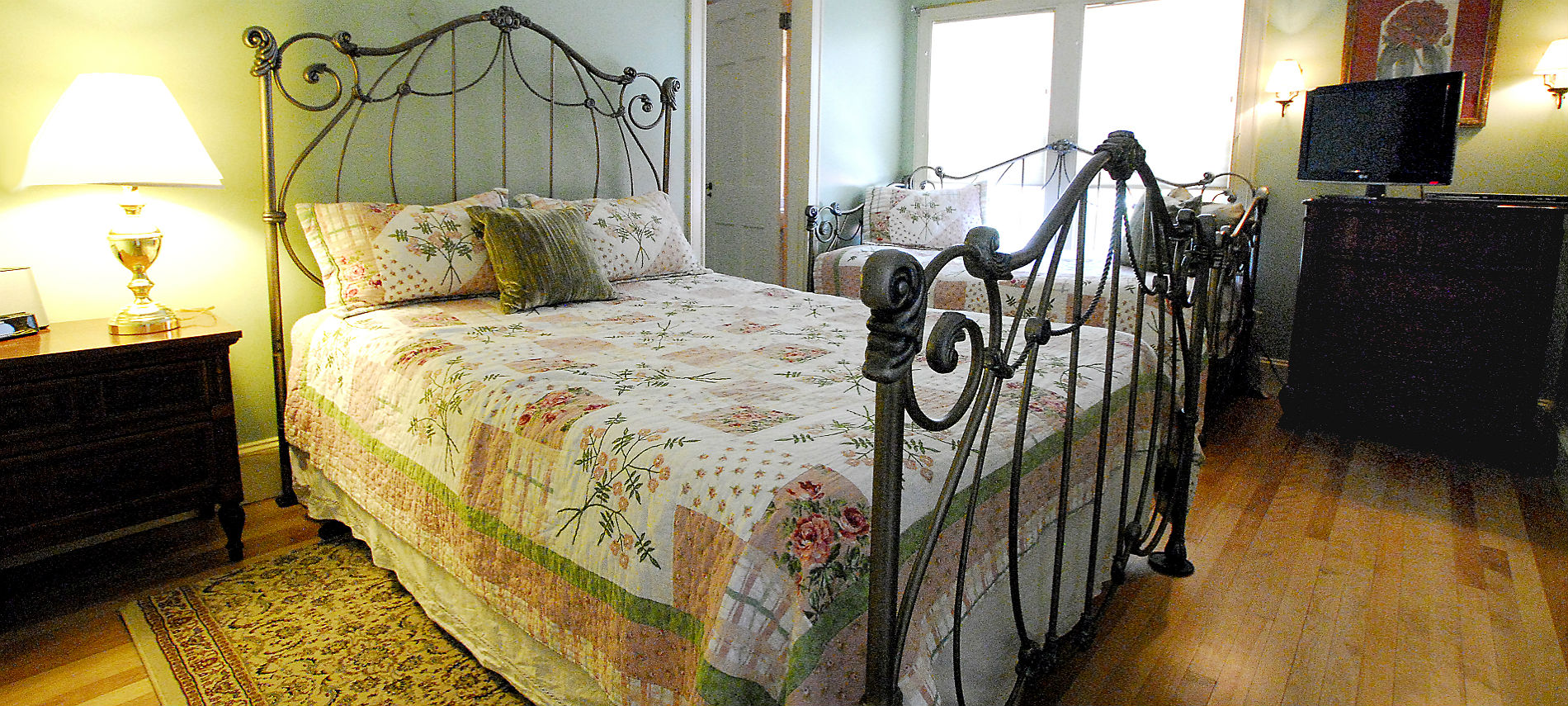 Cozy bedroom with an ornate iron bedstead made up with a floral quilt.